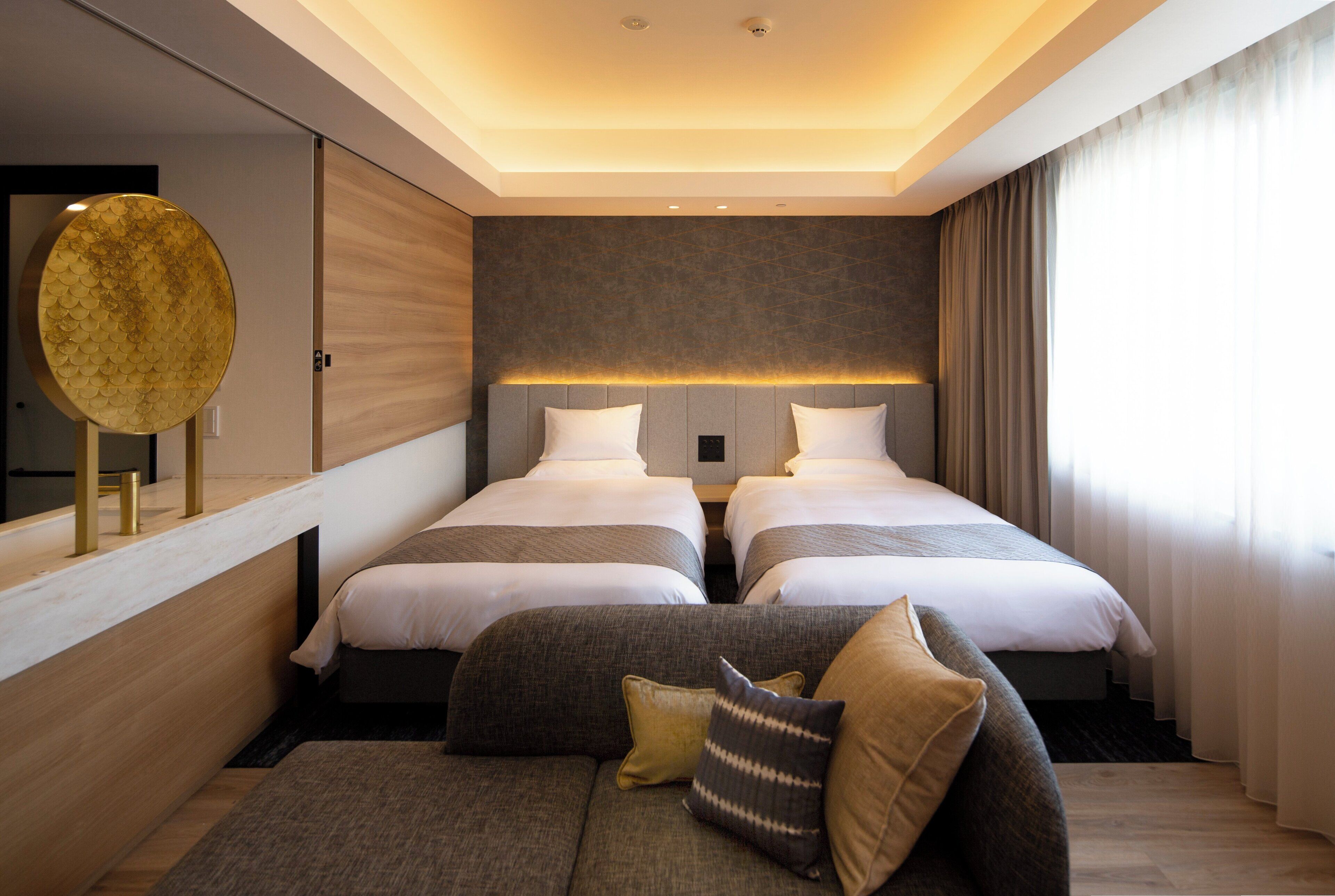 Habitación de hotel con dos camas, un sofá, un espejo grande y vistas al exterior.