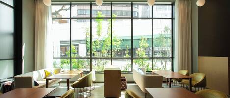 Un comedor moderno con mesas y sillas, ventanas amplias con cortinas y vistas a zonas verdes.