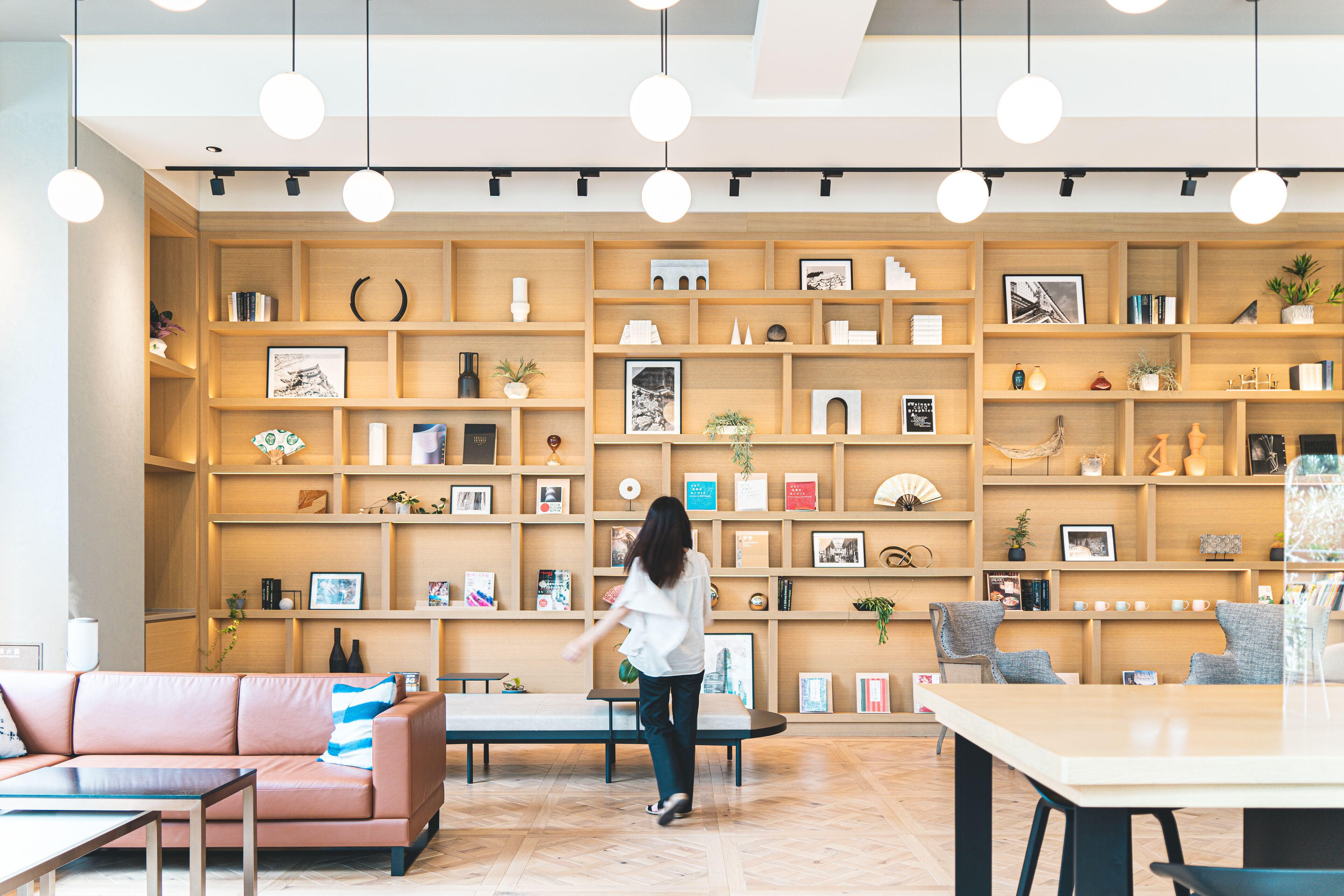 A modern interior with wooden shelving, a sofa, a table, and a person walking.