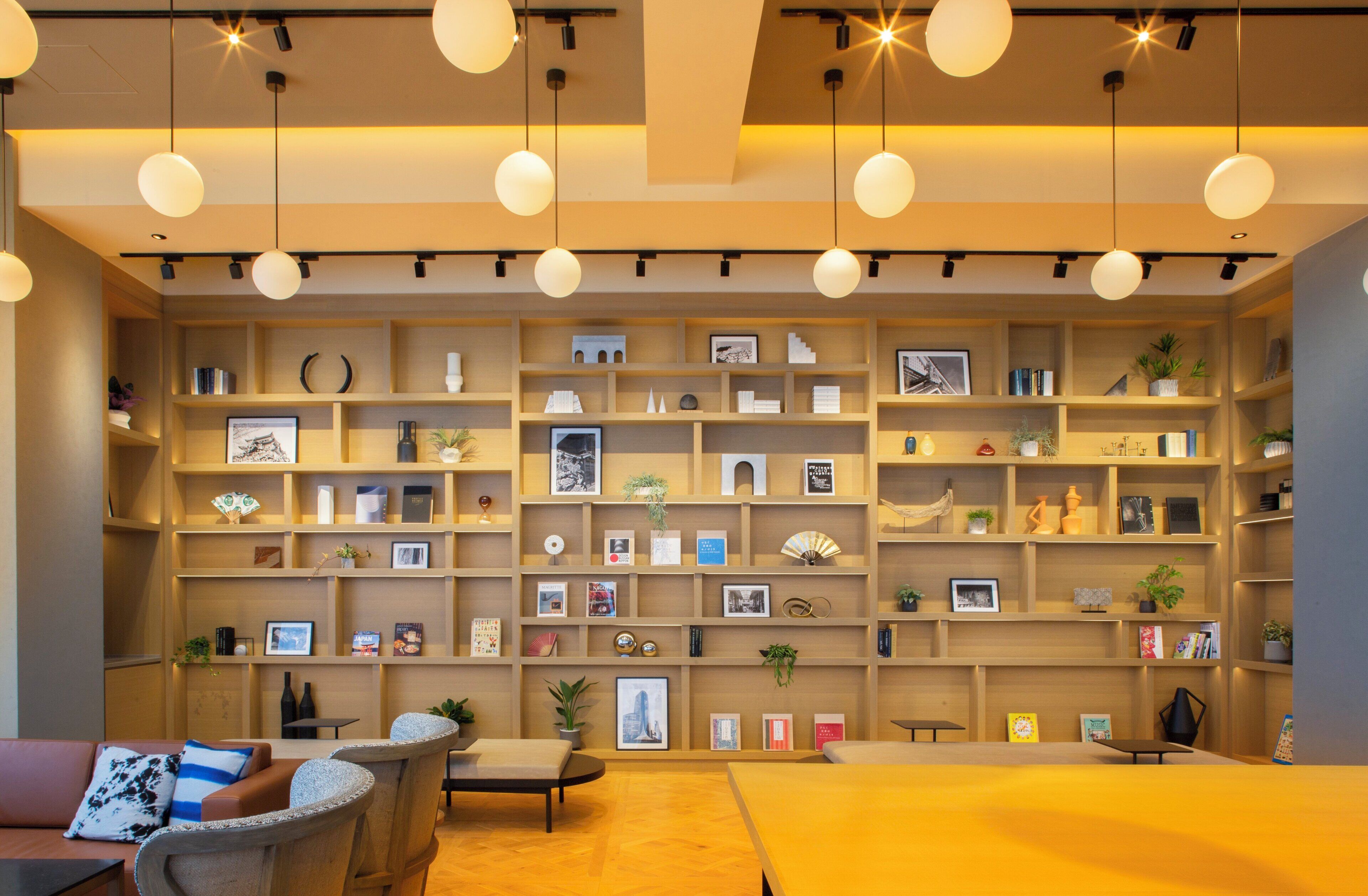 Um interior moderno com uma grande estante repleta de livros e objetos decorativos, uma área de estar com sofá e poltronas, e iluminação pendente.