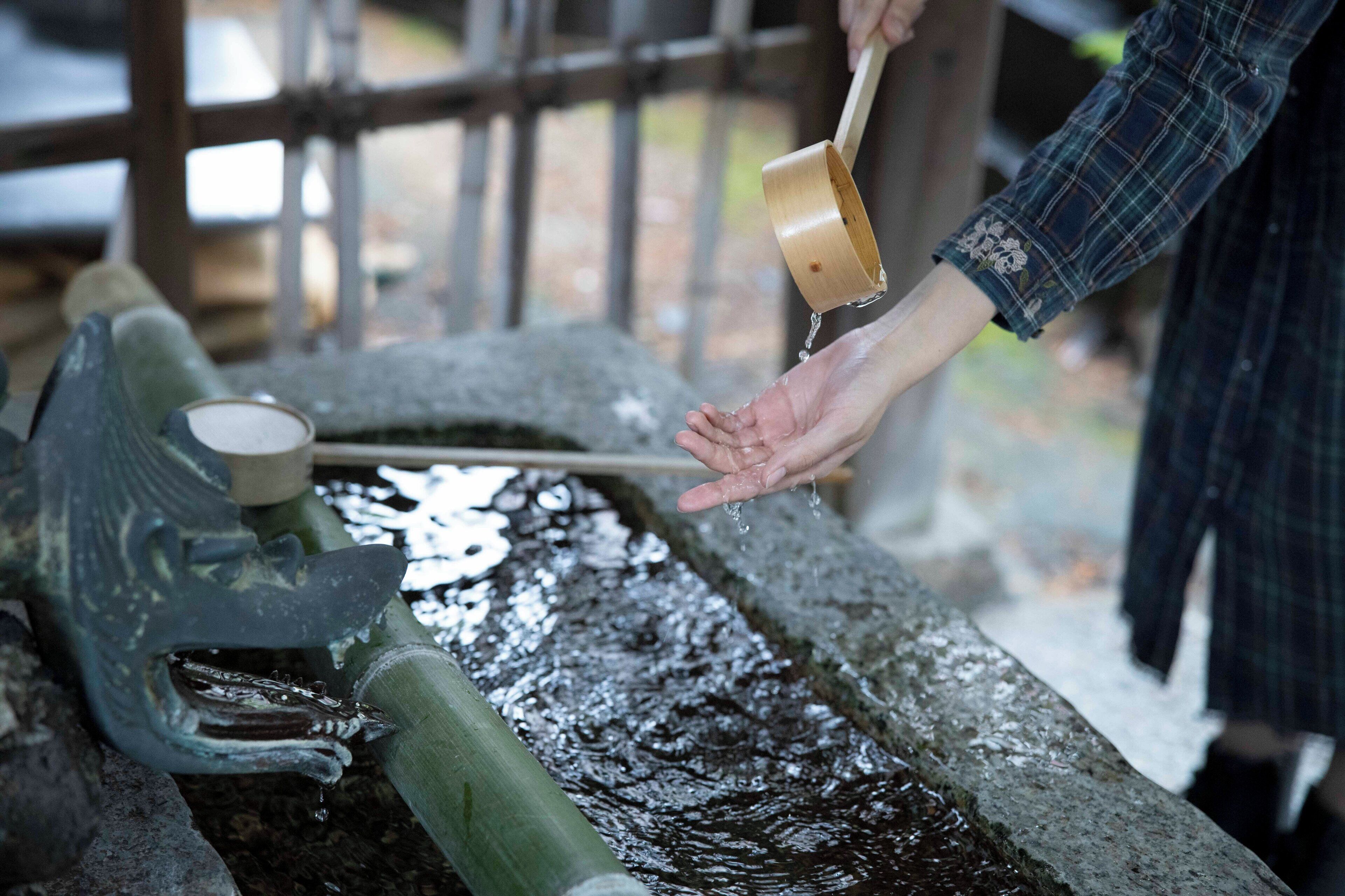 A person pouring water from a wooden container into a stone basin.