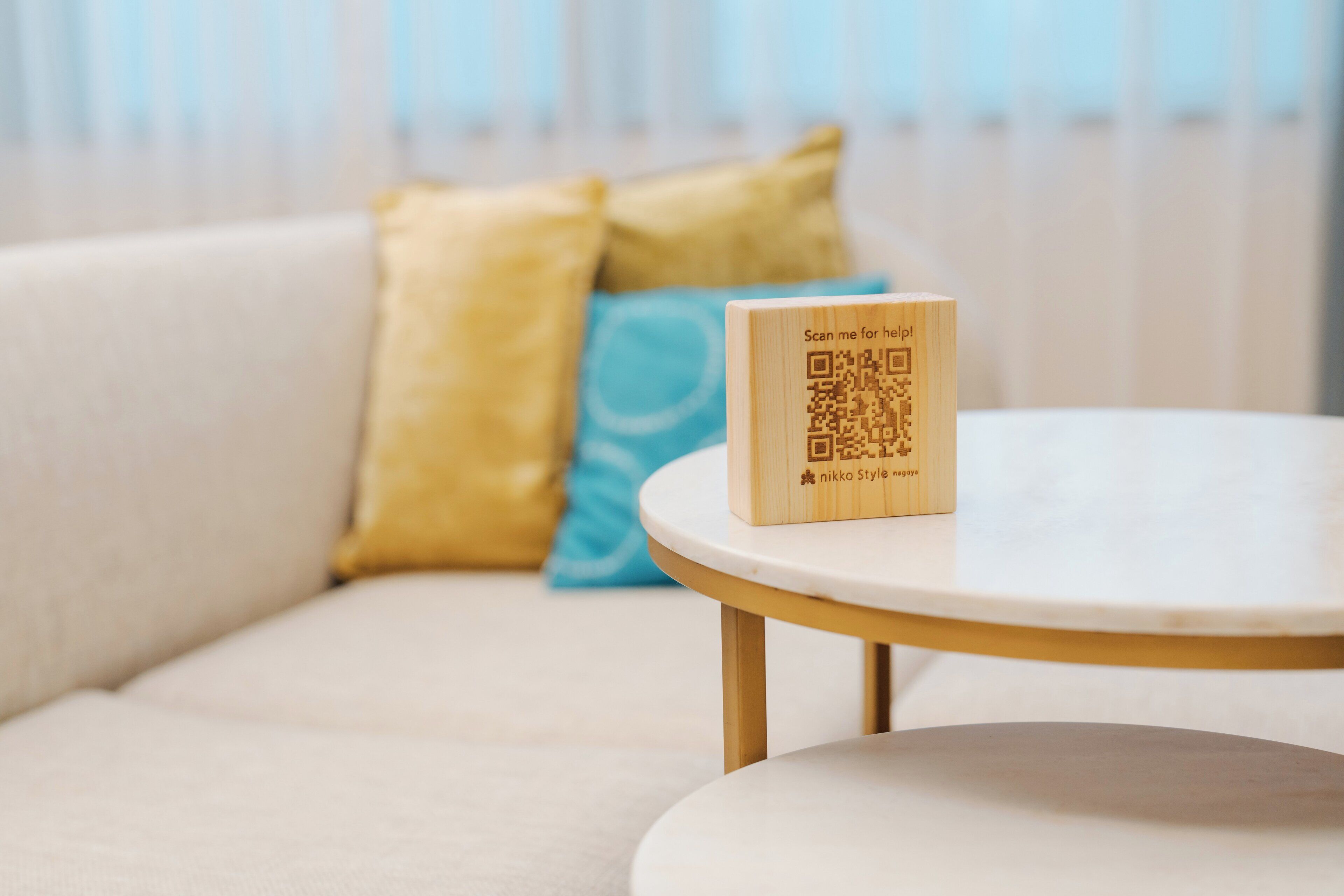 Une plaque en bois portant un code QR est posée sur une petite table ronde, avec un canapé et des coussins en arrière-plan.