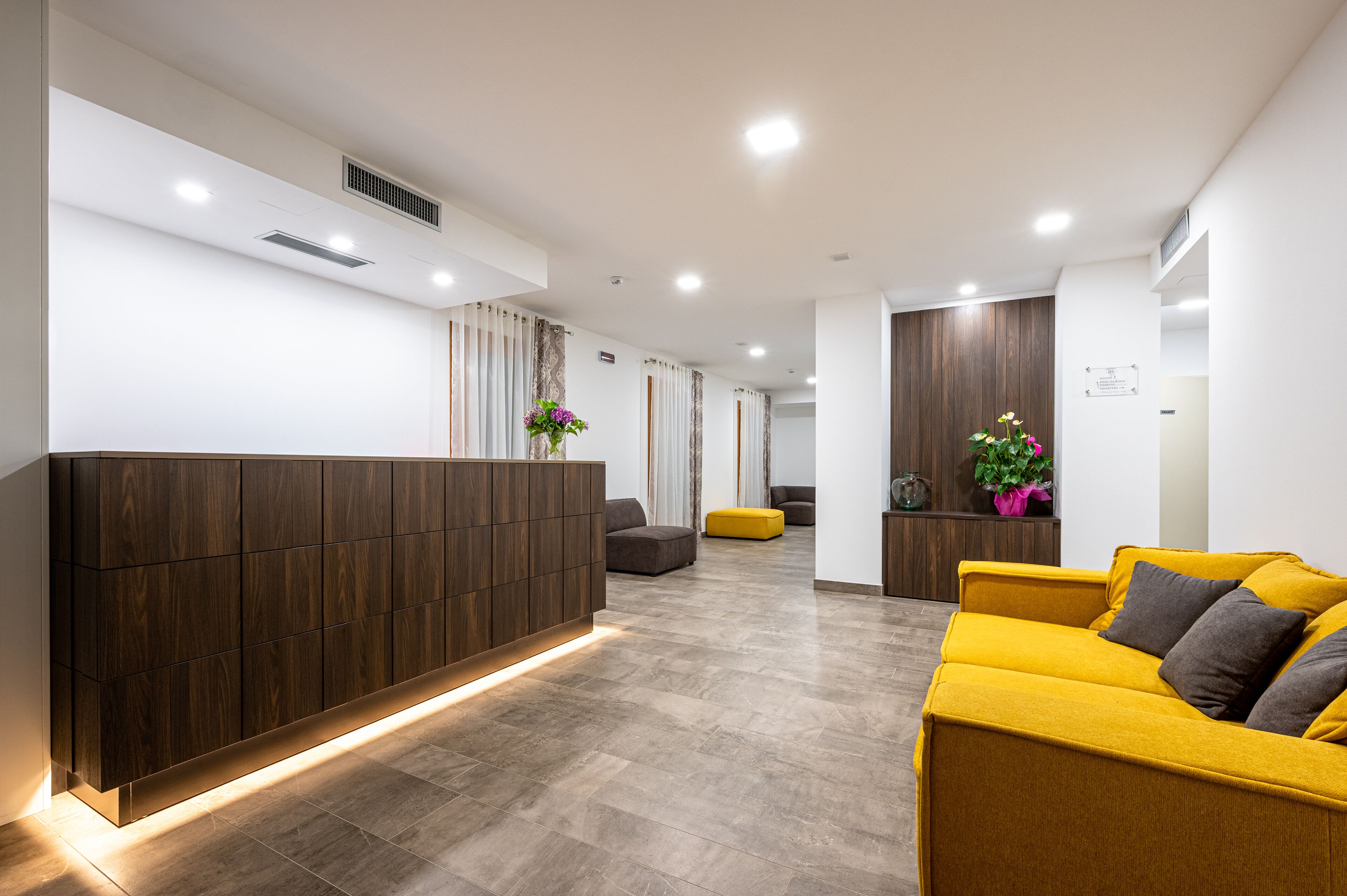 Un área de recepción moderna con un mostrador de madera, un sofá amarillo y un sofá gris.