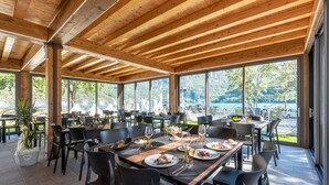 Un espacio de comedor al aire libre con vigas de madera, ventanas amplias y mesas dispuestas para comer.