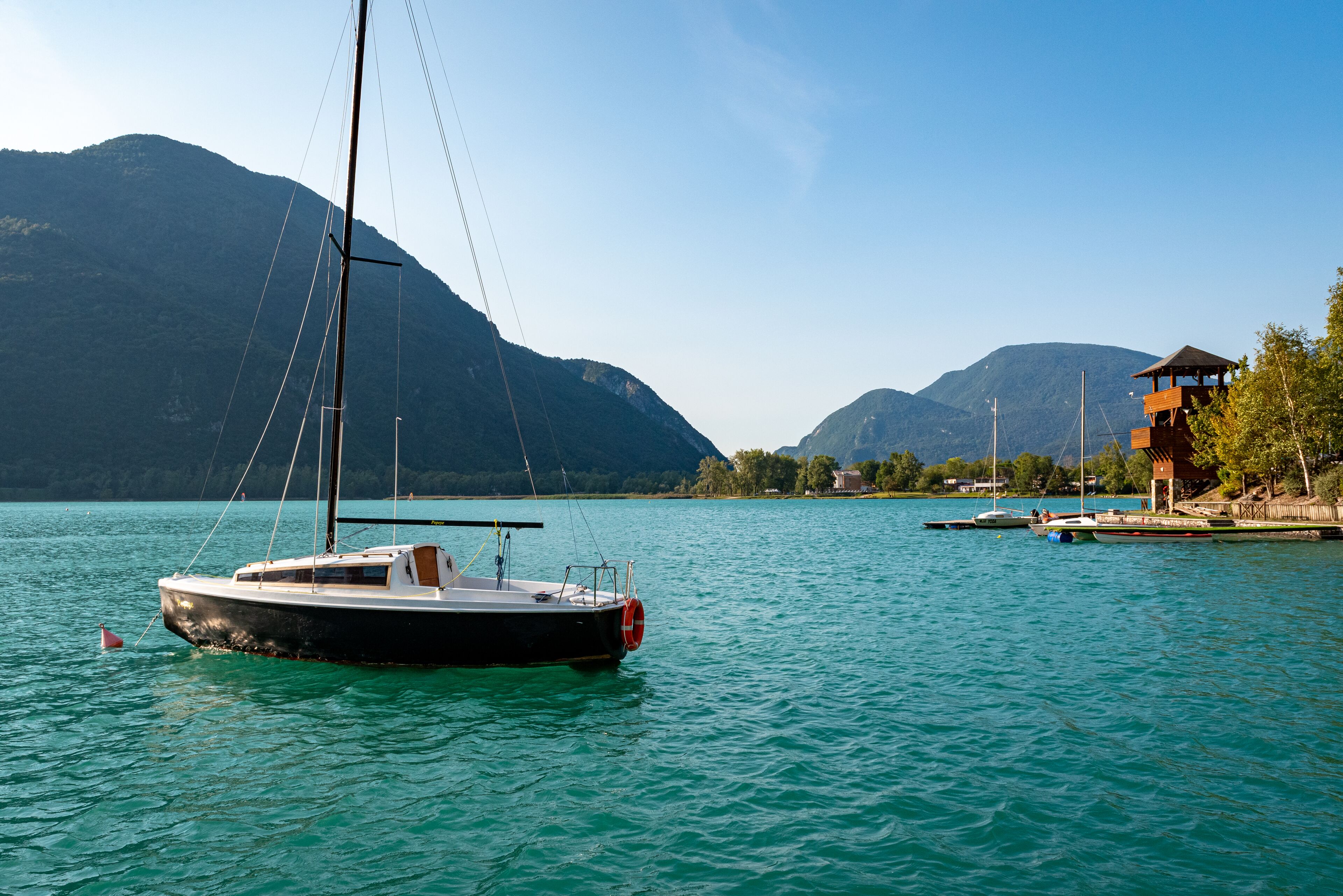 A sailboat docked at a calm lake with mountains in the background.