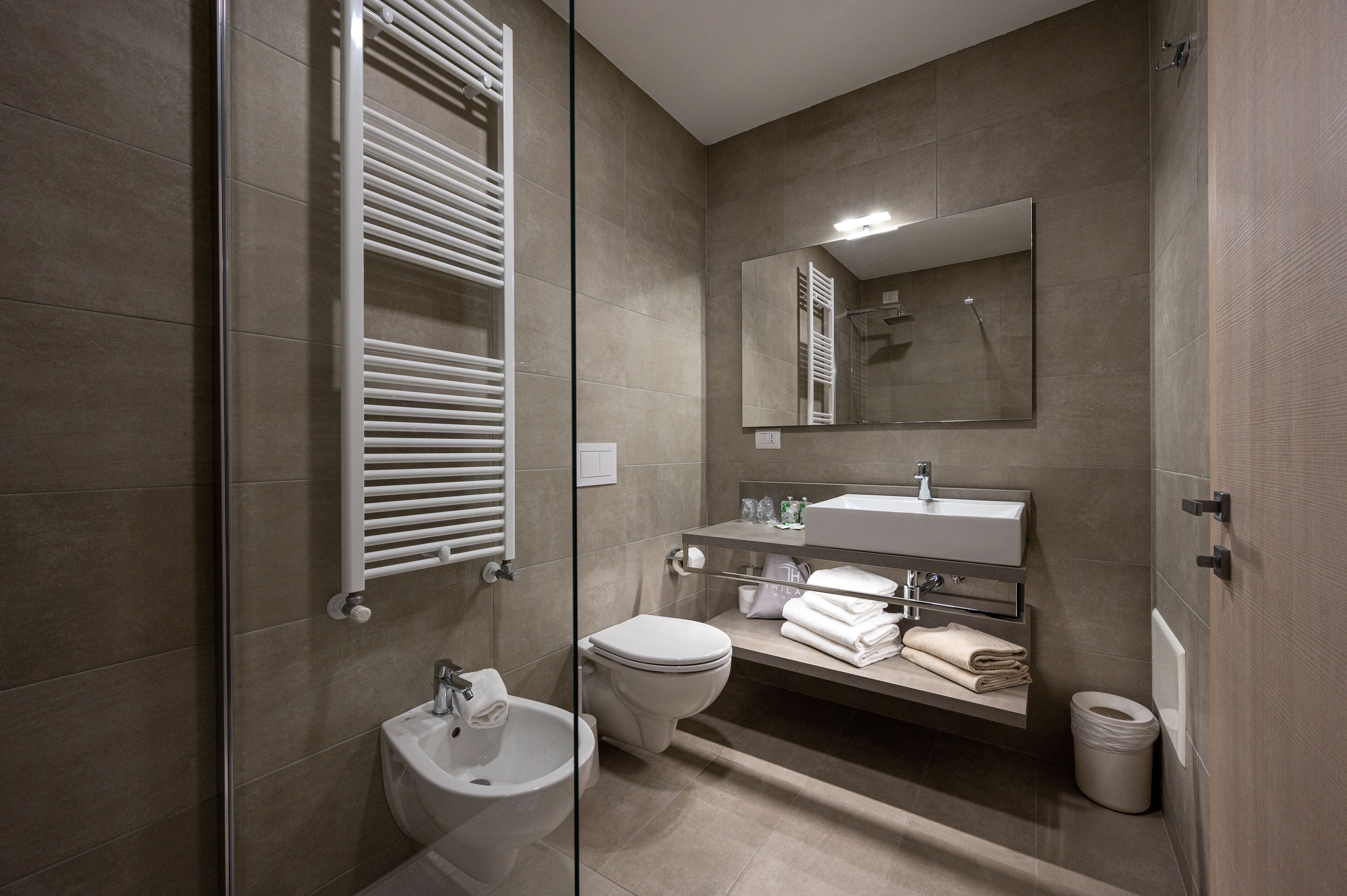 Un bagno moderno con box doccia in vetro, un WC bianco, un lavabo con specchio sopra e un porta asciugamani con asciugamani piegati.