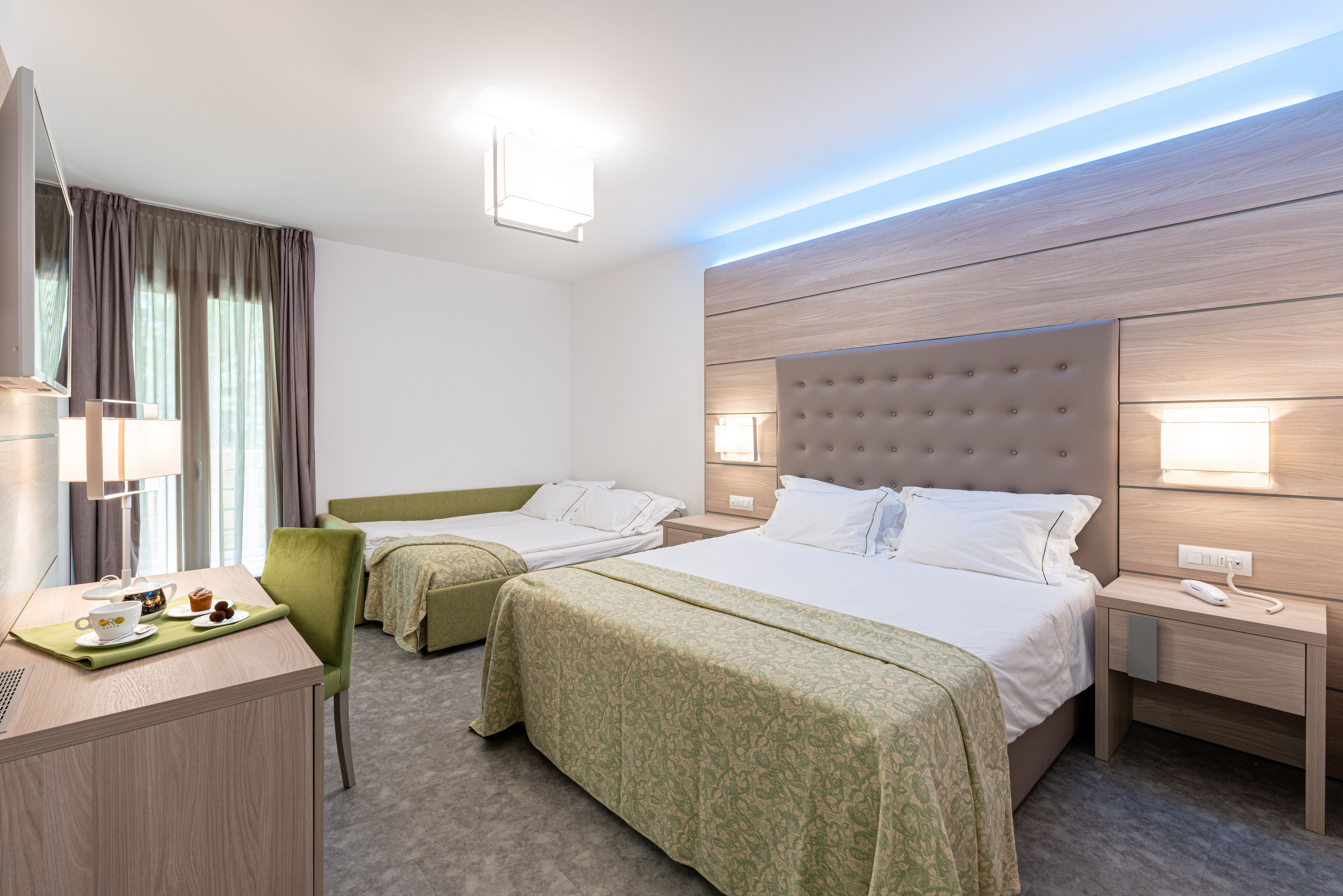 Habitación de hotel con dos camas individuales, un escritorio con lámpara, una silla y una mesita con una taza y un plato.