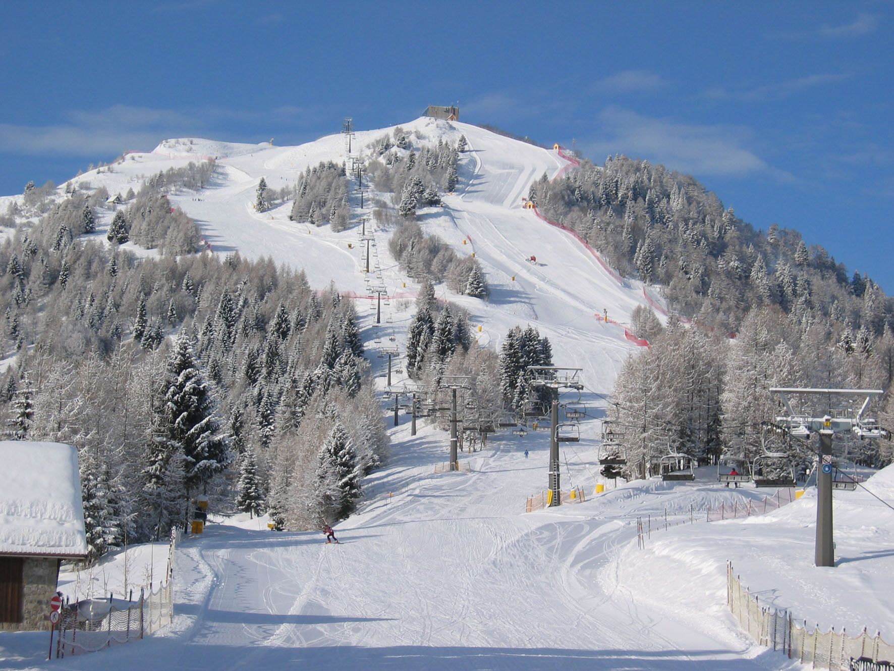 Een piste bedekt met sneeuw, met skiliften, bomen en een berg op de achtergrond.