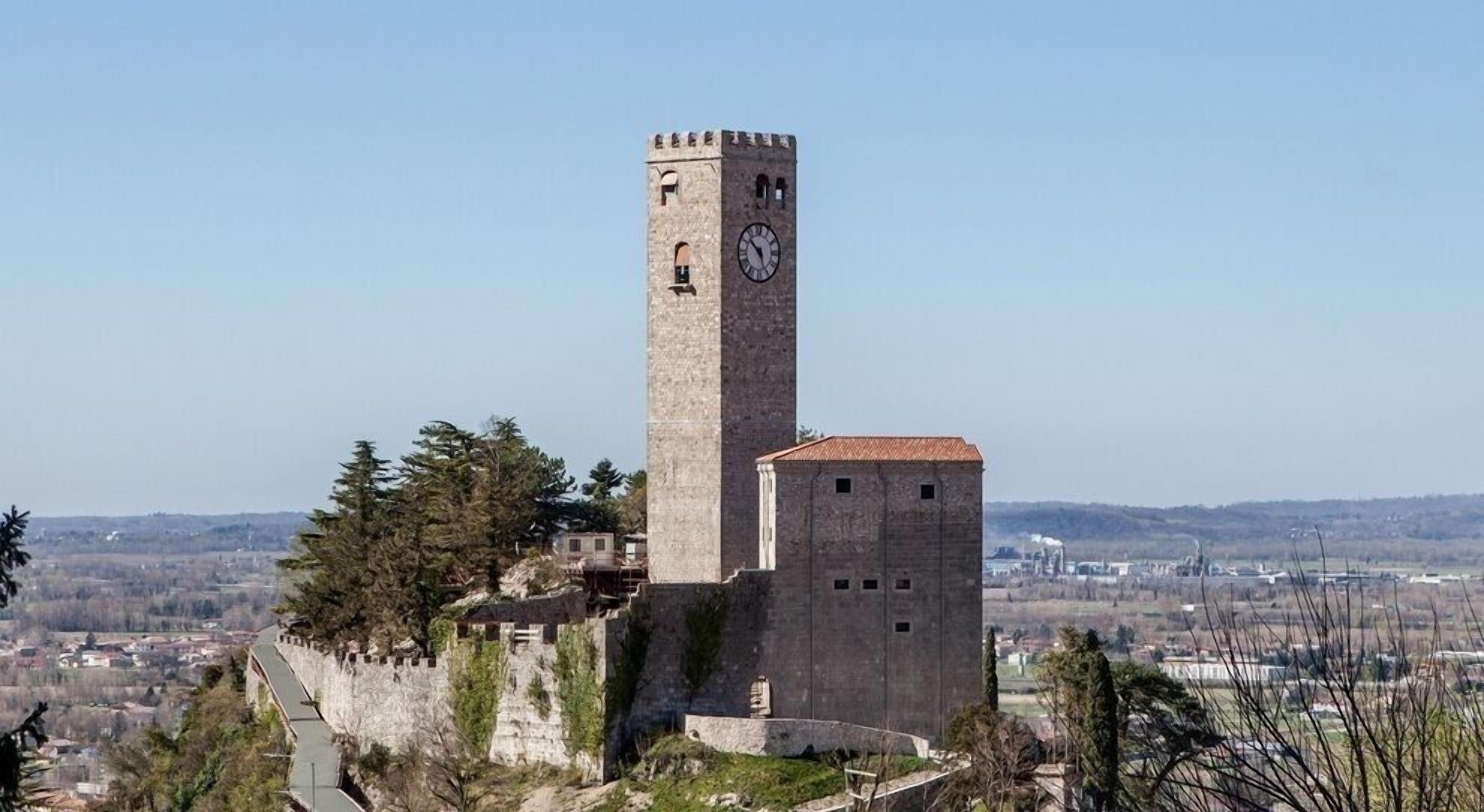 Une tour de pierre historique, dotée d’une horloge, entourée d’arbres et surplombant une ville.