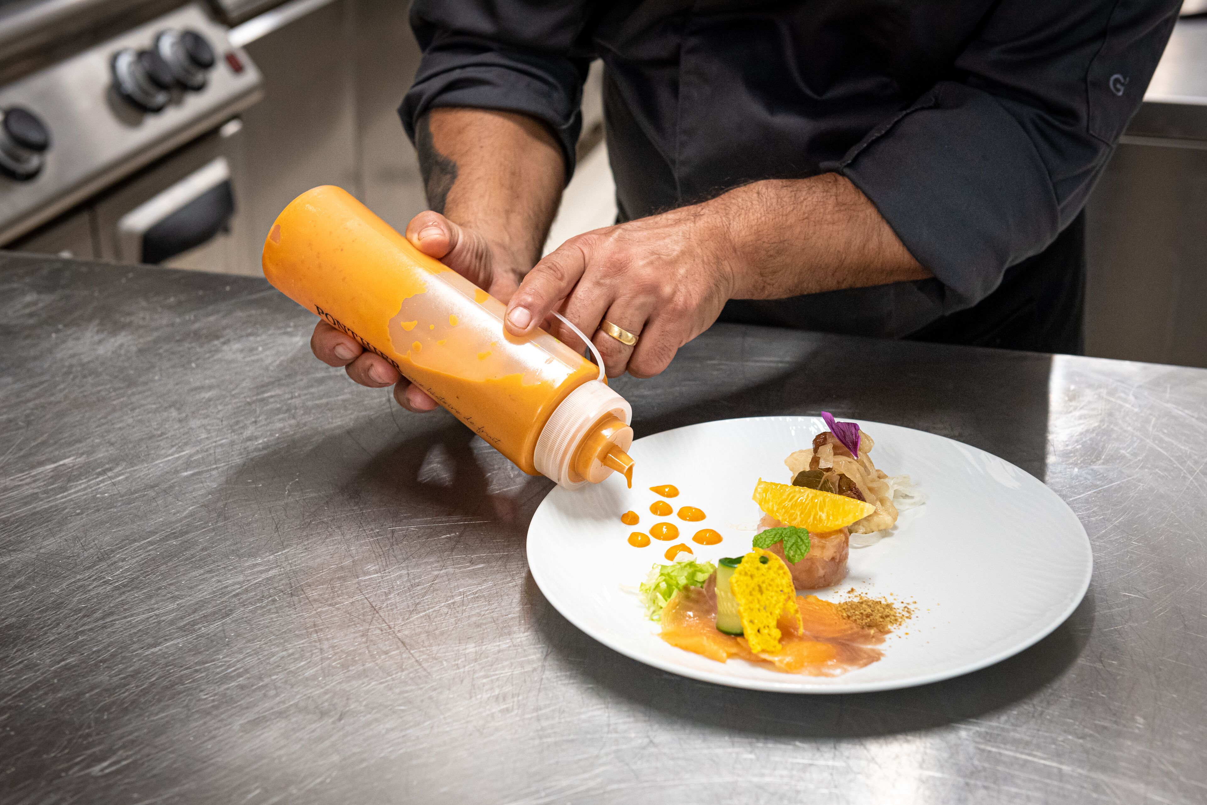 A chef pouring sauce onto a plated dish.