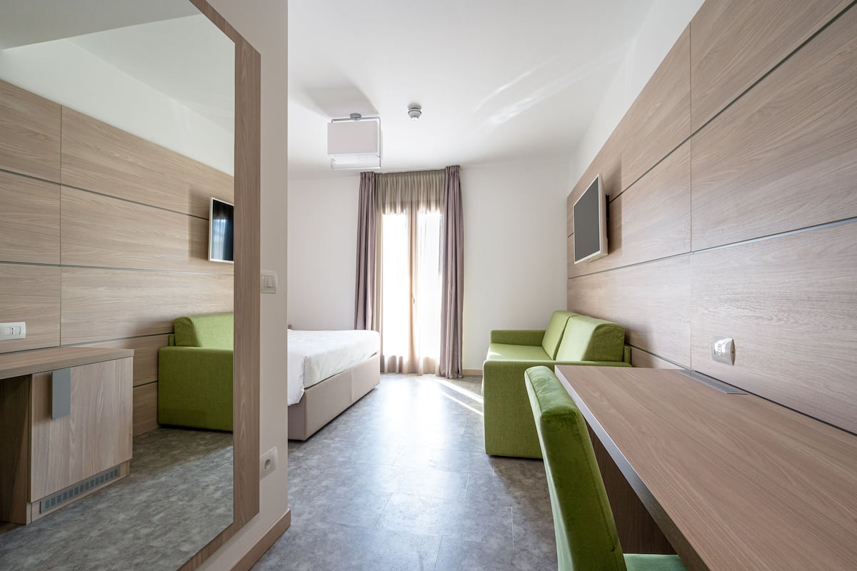 A modern hotel room with a bed, two green sofas, a small table, and a TV.