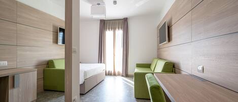 Una habitación de hotel moderna con una cama, dos sofás verdes, una mesita y un televisor.
