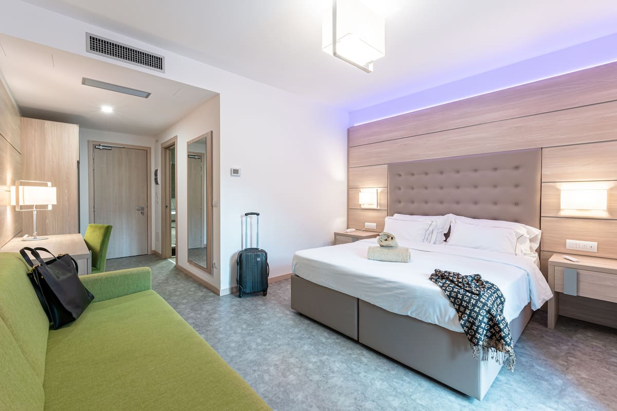 A hotel room with a bed, a green sofa, a suitcase, and a lamp.