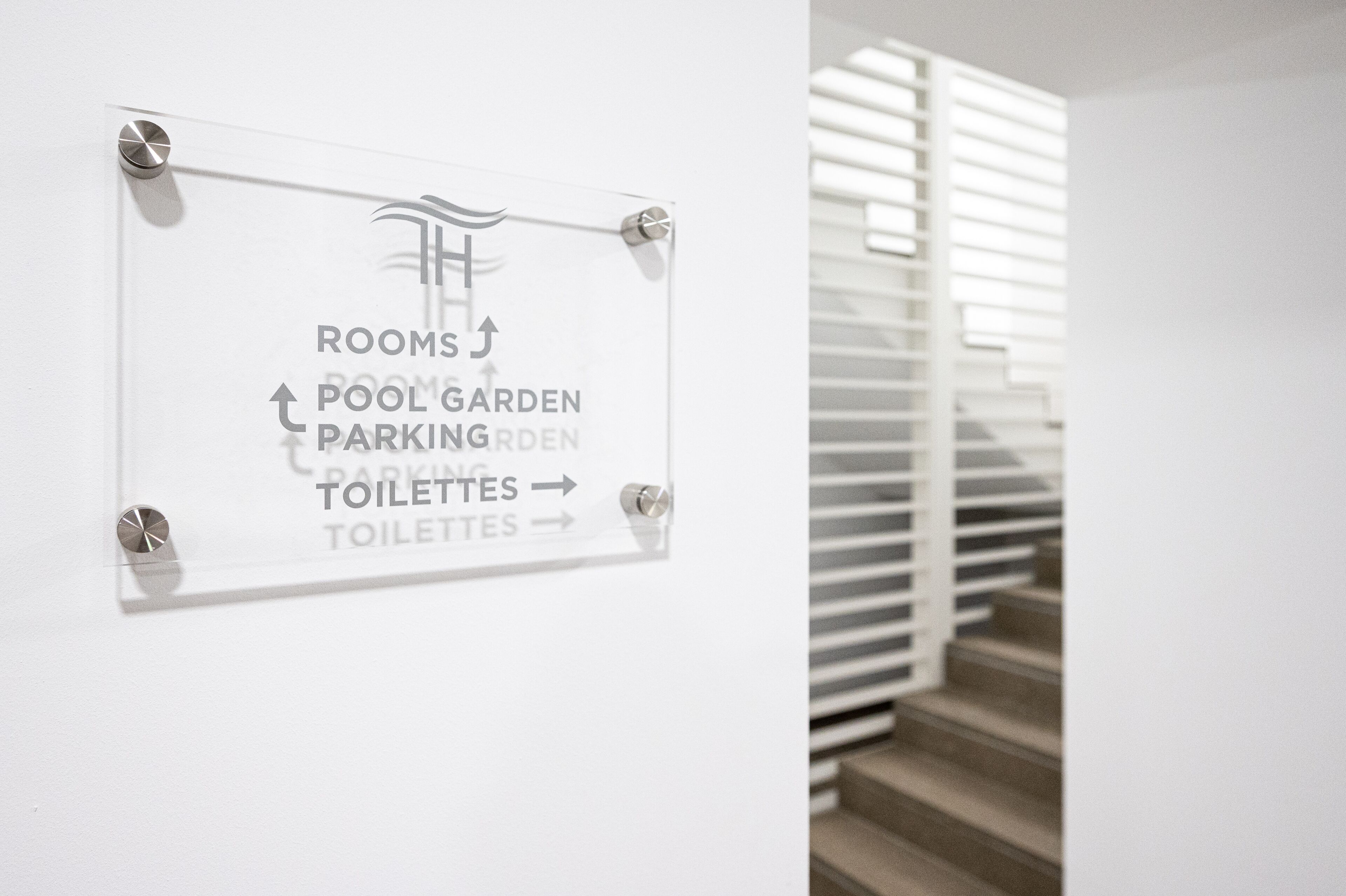 Señal direccional con flechas que indican la ubicación de habitaciones, piscina, jardín de estacionamiento y baños.