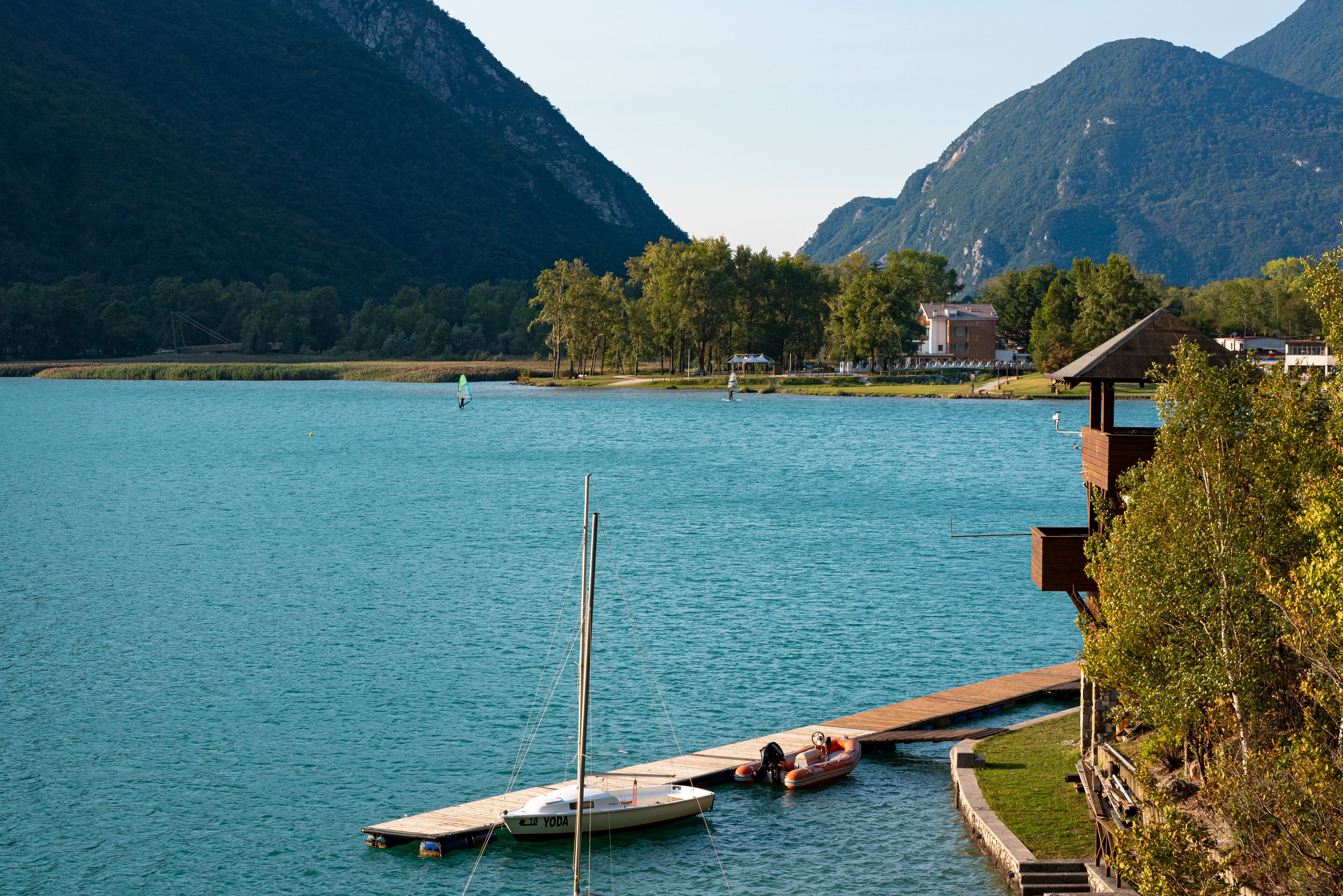 A lake with a dock, a small boat, and a building with a thatched roof.
