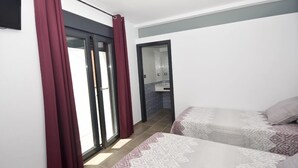 Et hotelværelse med to senge, en skydedør til en balkon og et badeværelse, der kan ses gennem døren.