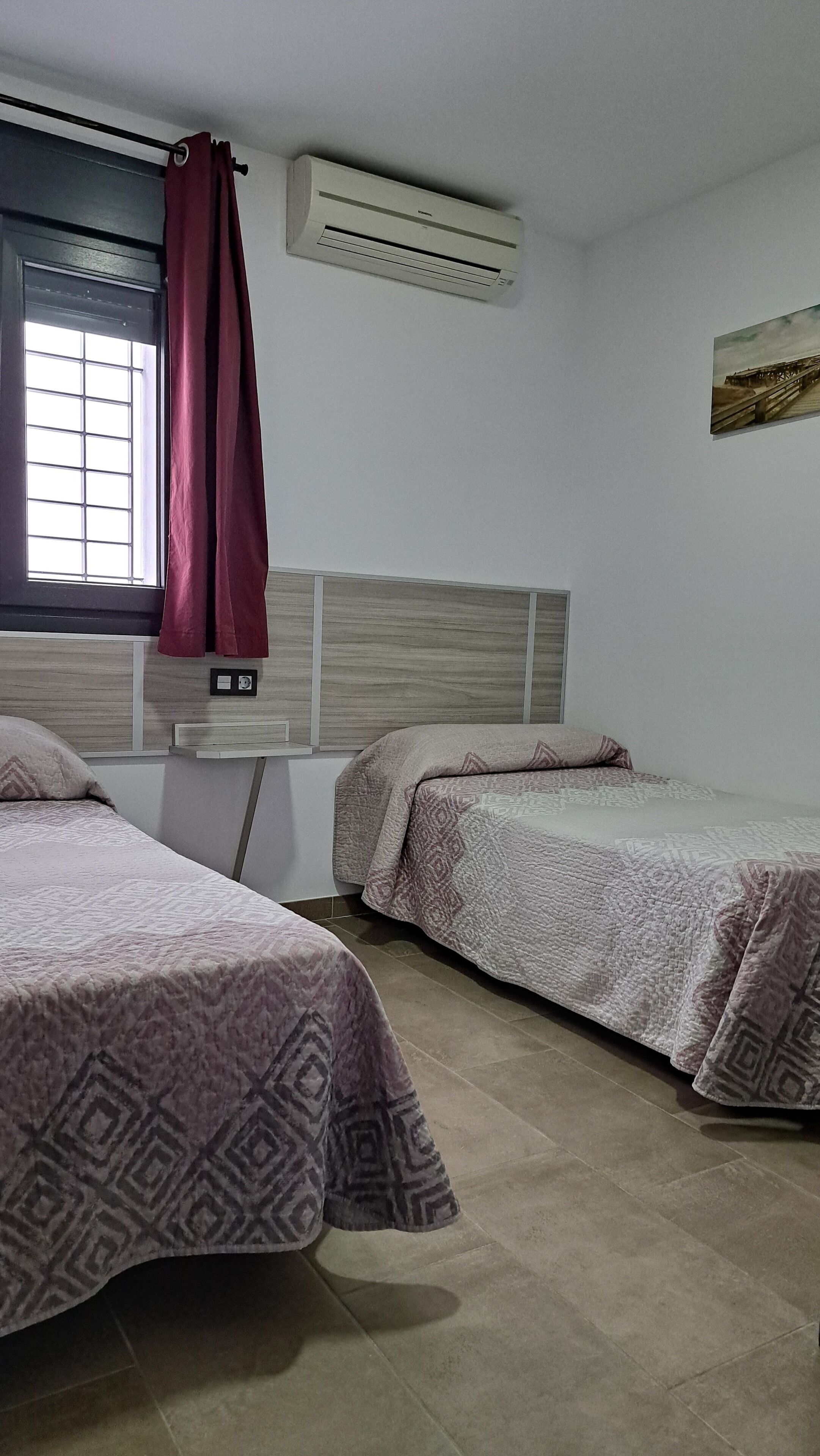 Une chambre avec deux lits, une fenêtre avec un rideau, un appareil de climatisation et un panneau de commande fixé au mur.