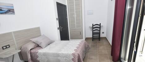 A bedroom with two beds, a wardrobe, a chair, and a window with curtains.