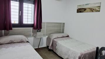 Una habitación con dos camas, una ventana con cortinas, un equipo de aire acondicionado y un cuadro en la pared.