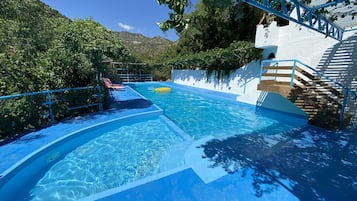 Una piscina al aire libre, sombrillas, sillones reclinables de piscina