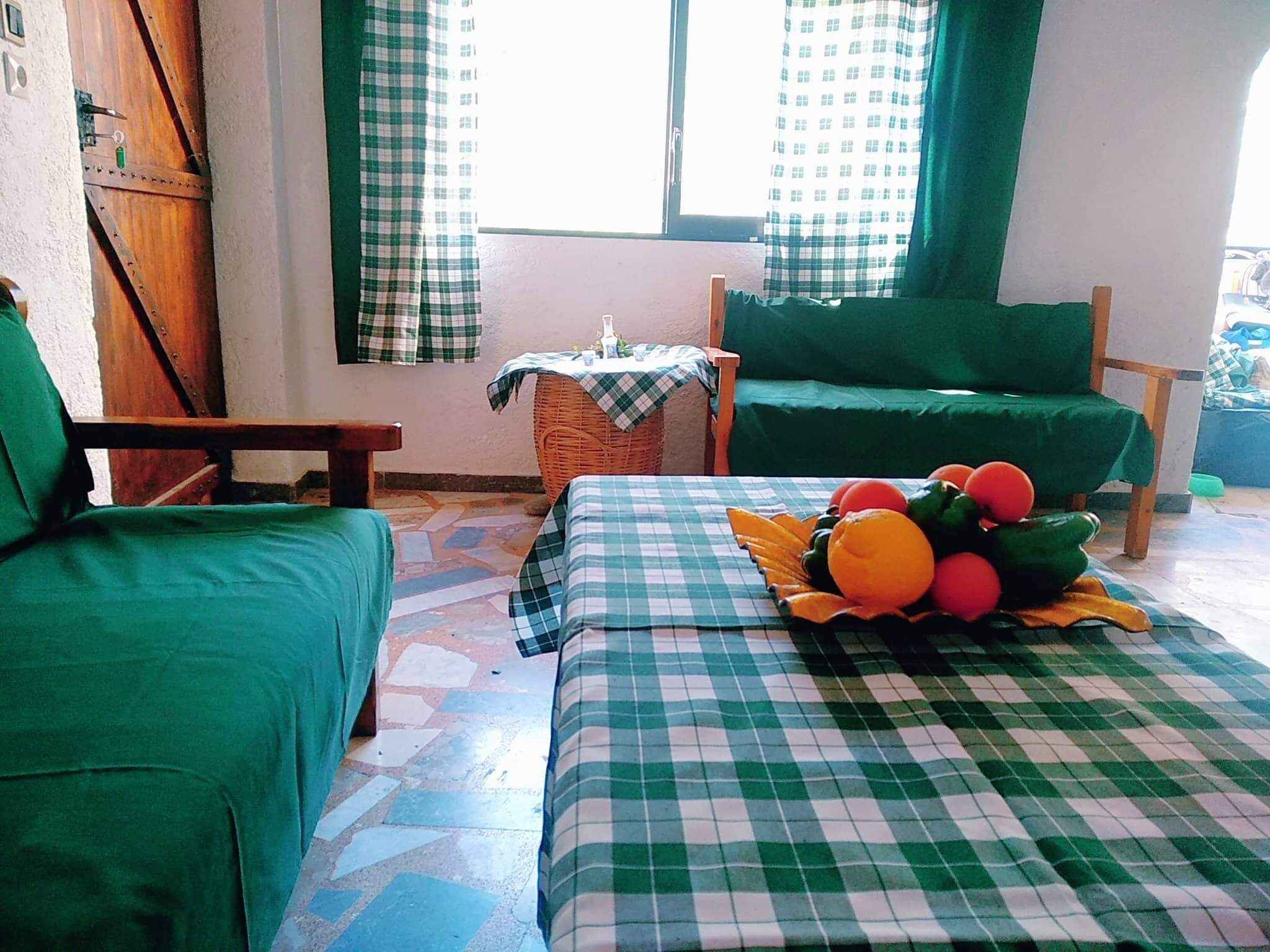 Una habitación con dos sofás tapizados en verde, una mesa a cuadros y una silla de mimbre.