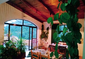 A dining area with a large arched window, wooden ceiling, and various potted plants. - Oleander's Garden (Ierapetra)