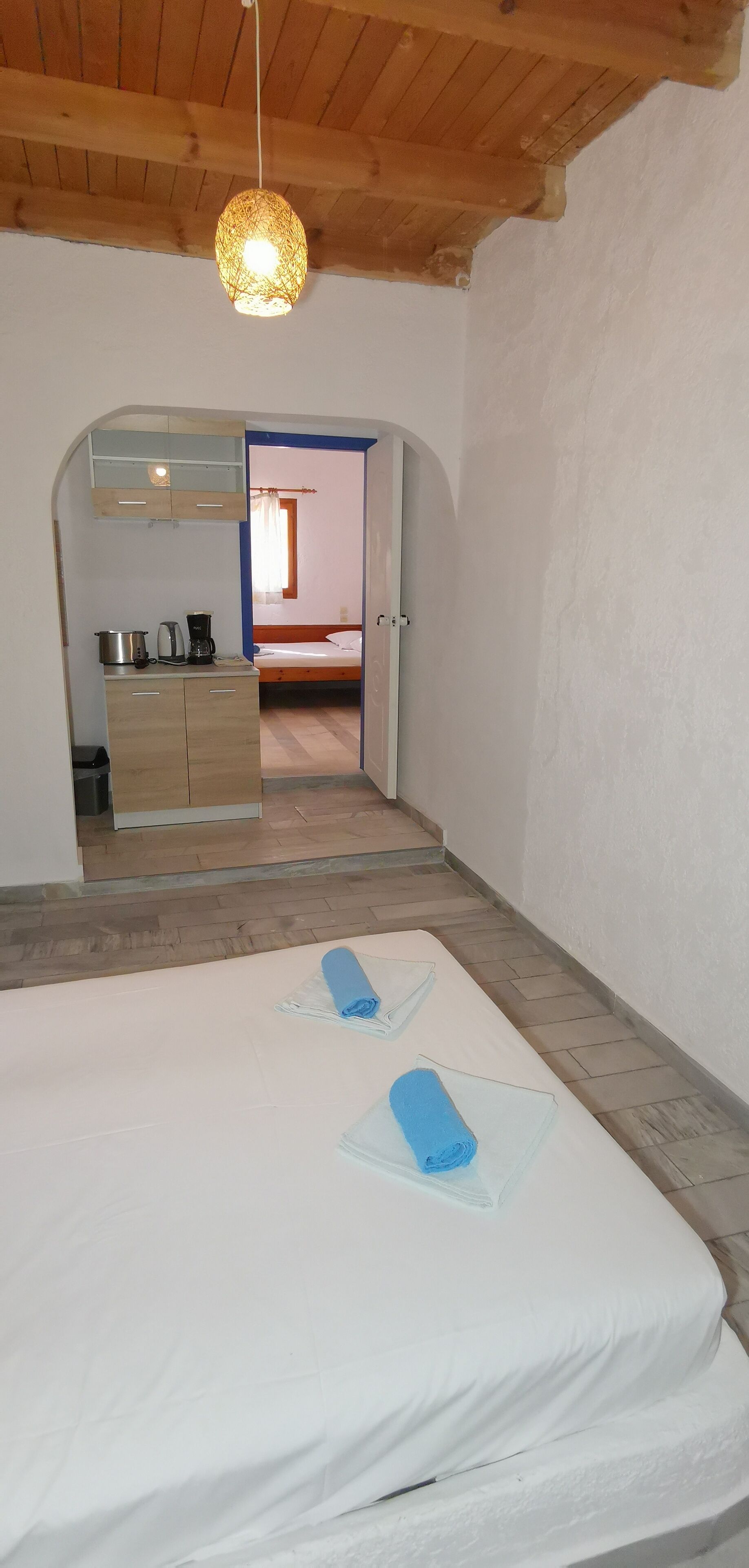 A bedroom with a bed, a small kitchenette, and a wooden ceiling.