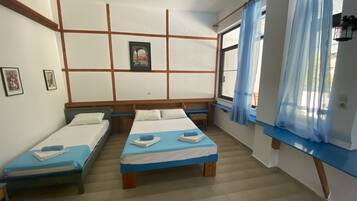 Una habitación con dos camas individuales, cabecera de madera, una mesita y una ventana con cortinas azules.