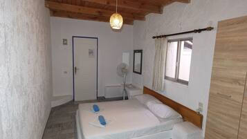 A bedroom with a bed, a bedside table, a mirror, a window with curtains, and a wooden wardrobe.
