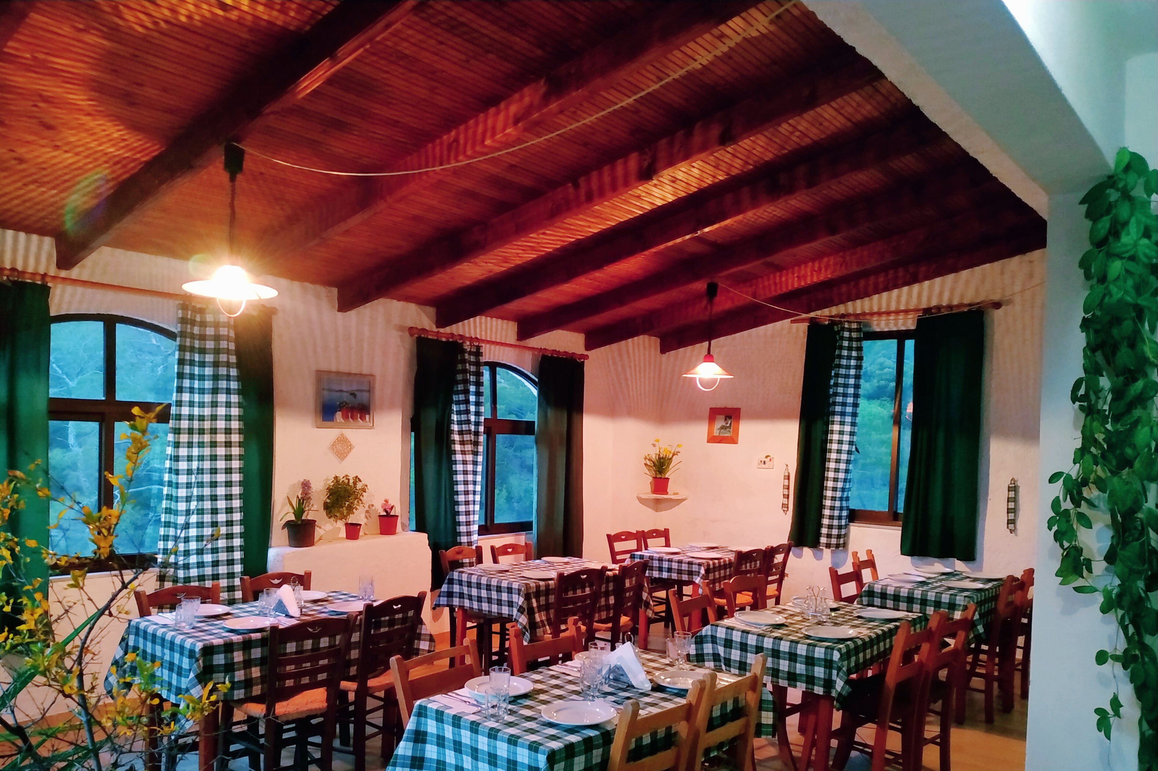 A restaurant with checkered tablecloths, wooden beams, and potted plants.