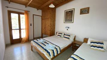 A bedroom with two beds, wooden flooring, a wooden ceiling, a door, and a window with curtains.