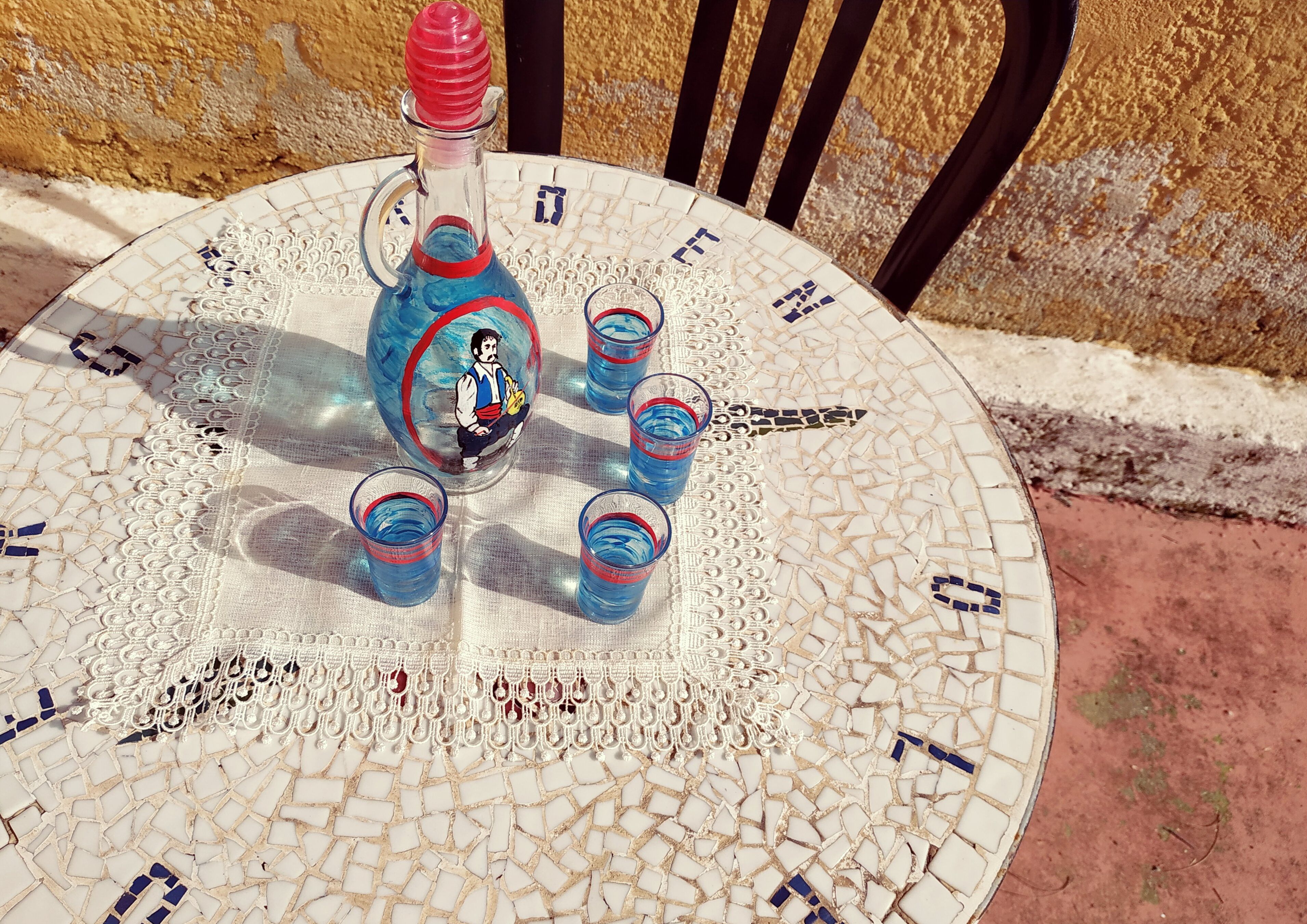 Una mesa redonda con un diseño de mosaico, una botella con tapón rojo y cuatro vasos.