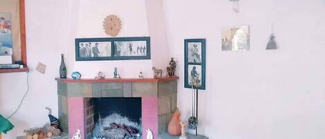 Una sala de estar con chimenea, una mesa a cuadros y diversas decoraciones en las paredes.