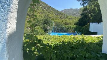 A view through an arched doorway of a pool area surrounded by lush greenery and a mountainous backdrop.