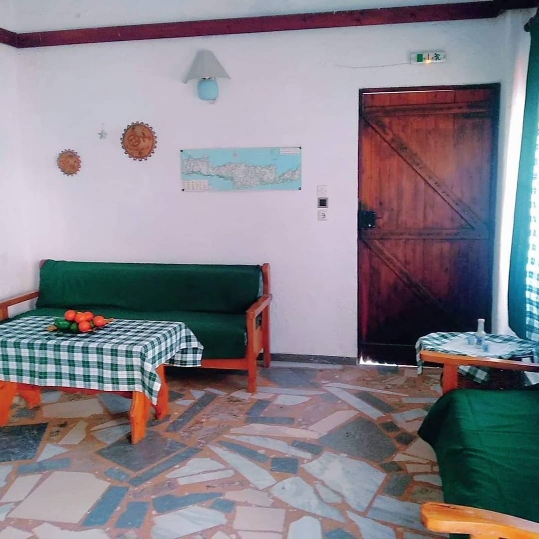 A room with a green sofa, a small table with a checkered tablecloth, a map on the wall, and a wooden door.