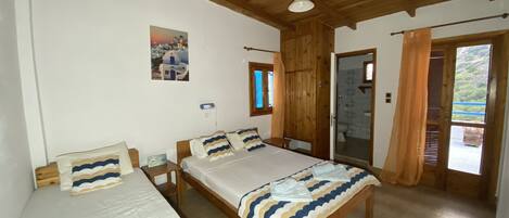 A room with two beds, wooden flooring, a wooden ceiling, a window with curtains, and a door leading to a bathroom.