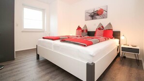 Un dormitorio moderno con una cama grande, una mesita de noche con lámpara, una ventana y una obra de arte colgada en la pared.