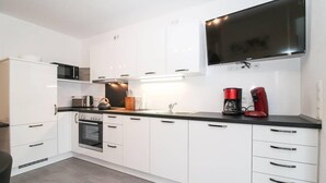 Una cocina moderna con armarios blancos, un microondas, una cafetera y un televisor de pantalla plana montado sobre la encimera.