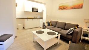 A modern living room with a sofa, a coffee table, and a kitchen in the background. - Victus Apartamenty - Riviera (Sopot)