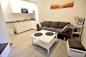 A modern living room with a sofa, a coffee table, and a small kitchen area with white cabinets and a microwave.