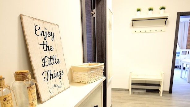 A hallway with a white dresser, a sign that says "Enjoy the Little Things," and a bench. - Victus Apartamenty - Riviera (Sopot)