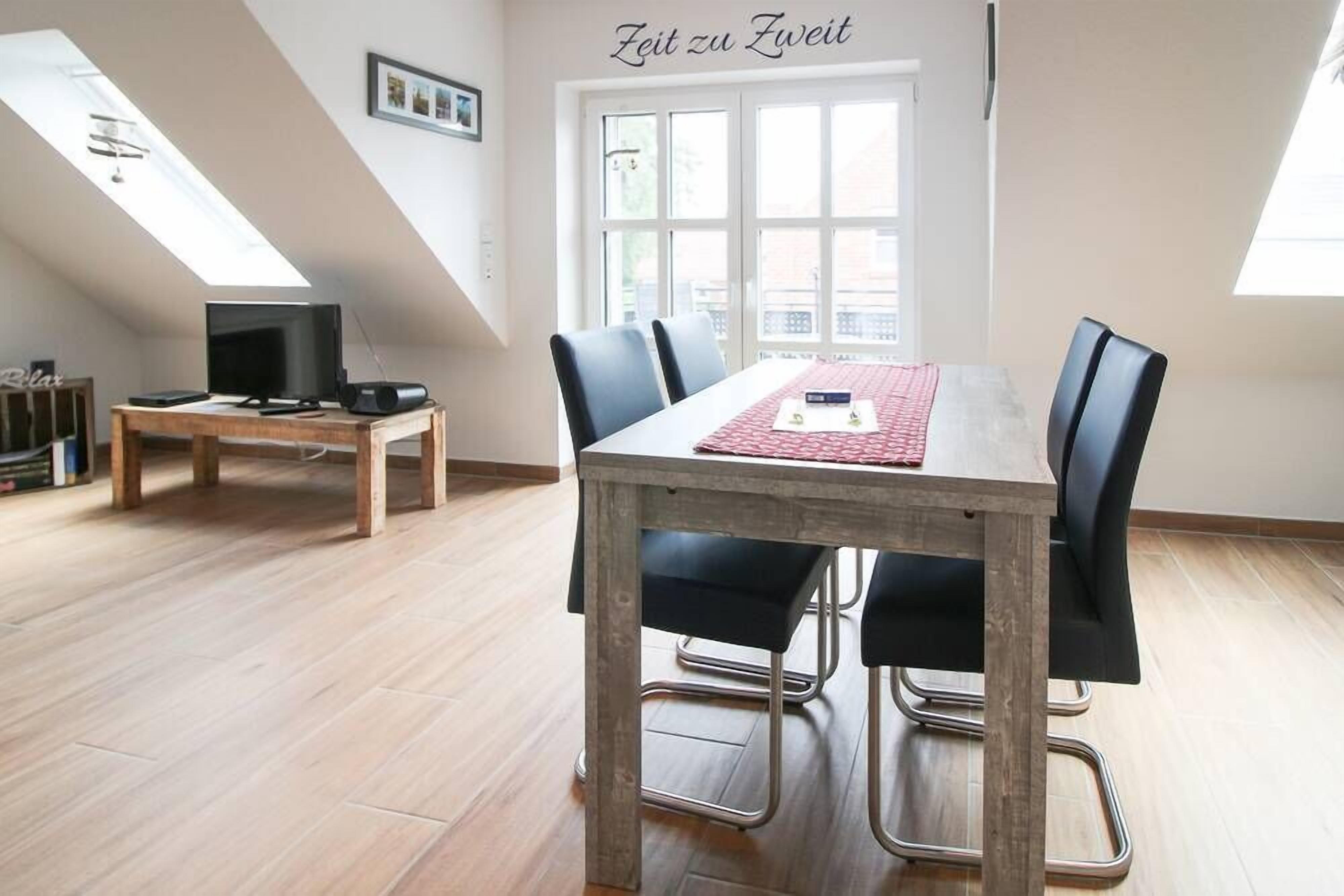 A dining area with a table, chairs, and a television. There is a window with a view outside.