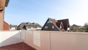 A rooftop terrace with a red-tiled floor, white railing, and a view of neighboring houses. - Muckelstuuv (Krummhoern)
