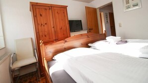 A bedroom with two beds, a wooden wardrobe, a television, and a chair. - Muckelstuuv (Krummhoern)