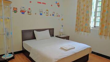 Una cama bien hecha con edredón blanco y almohadas, una mesita de noche con una lámpara, una pared con adornos de Hello Kitty y una ventana con cortinas.