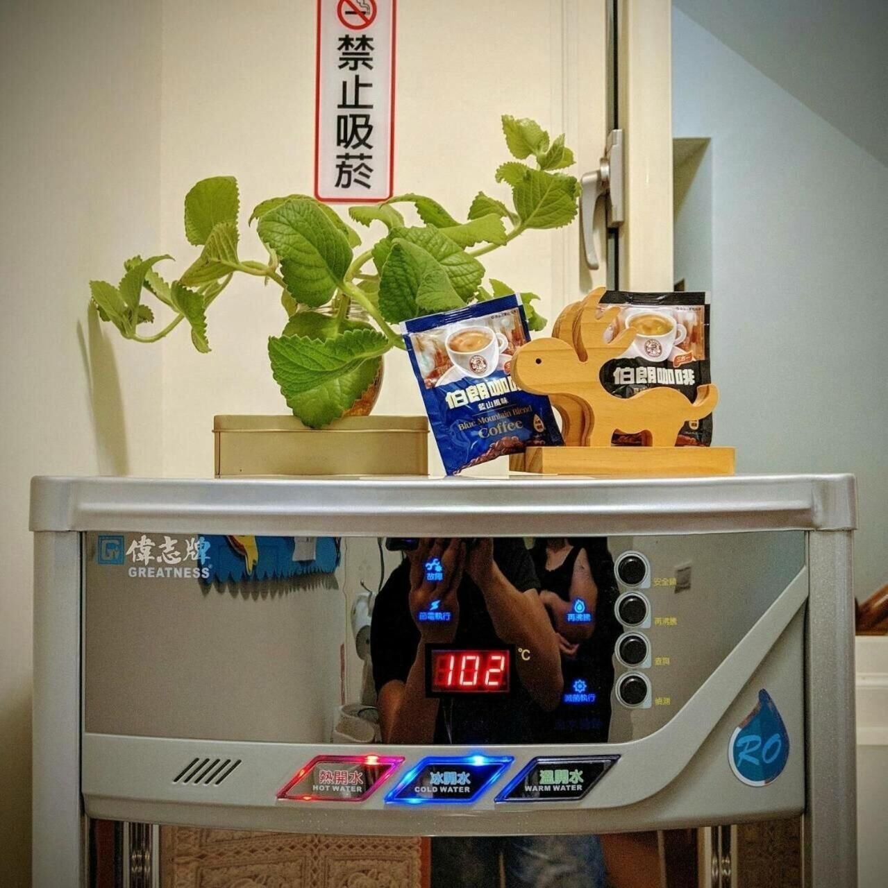 A coffee machine with a digital display, a plant, and a coffee bag on top.