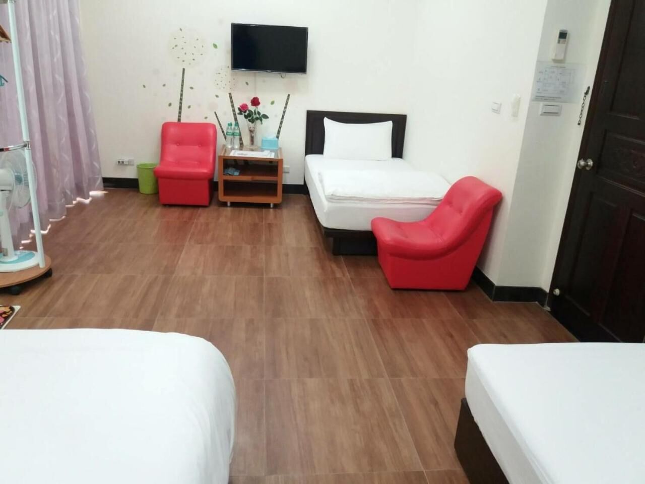 Une chambre d’hôtel avec deux lits, un téléviseur, une petite table ornée d’un vase de fleurs et un fauteuil rouge.