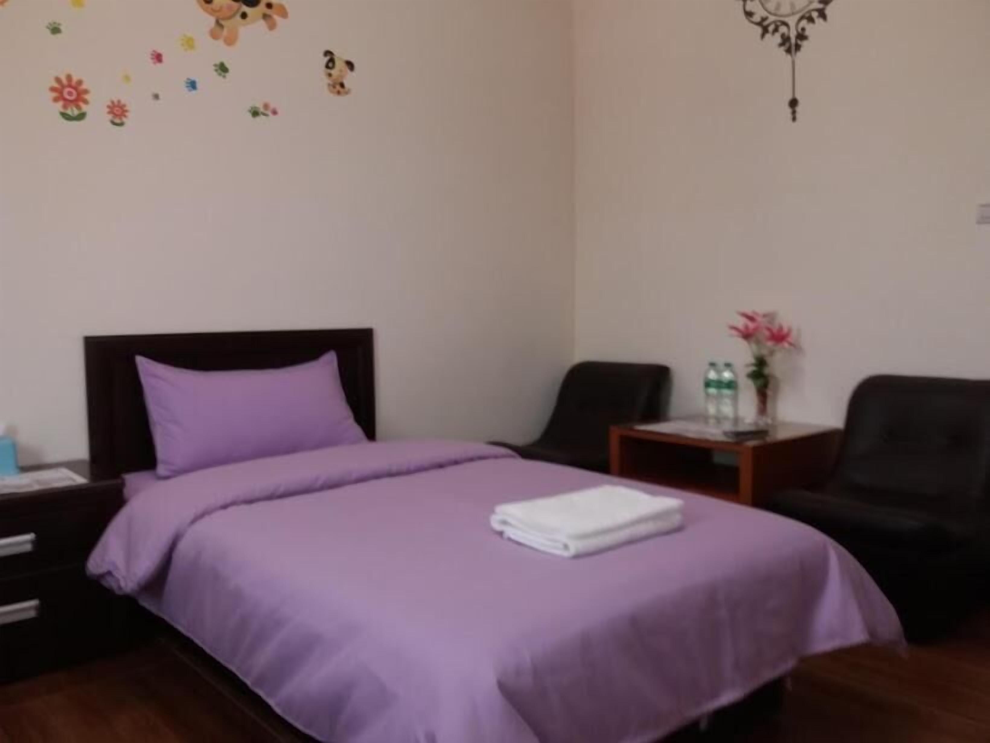 Una habitación de hotel con una cama, una mesita de noche, una silla y una pequeña mesa con un florero.