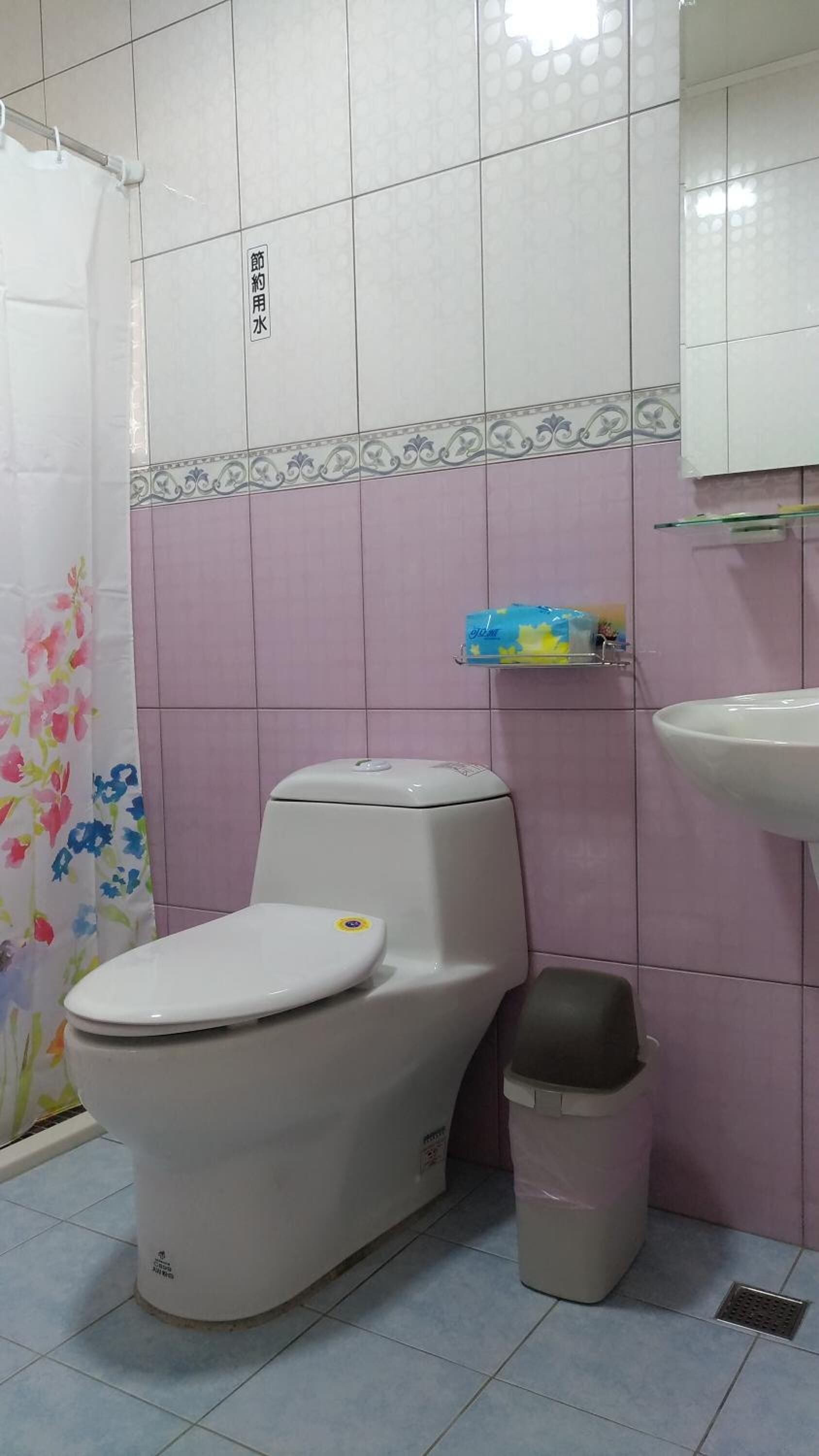A bathroom with a toilet, a trash bin, a shower curtain, and a sink.