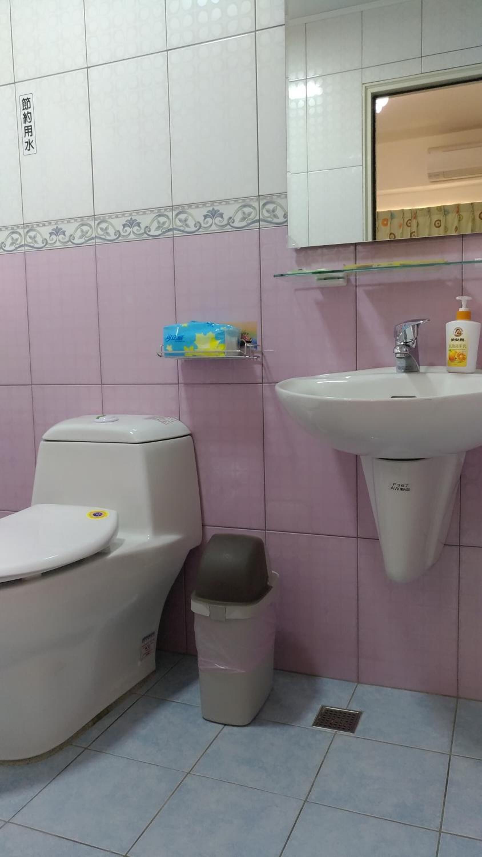 A bathroom with a toilet, a sink, and a trash bin.